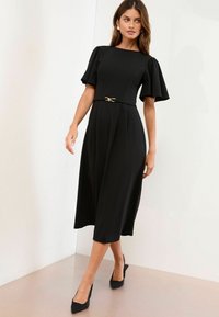 Rochie midi neagră, cu mâneci scurte tip puff, strânsă în talie cu un cordon subțire cu un accent auriu. Material neted și siluetă în formă de A.