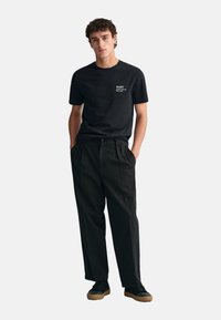 Camiseta negra de algodón con logo blanco en el lado izquierdo del pecho, combinada con pantalones negros holgados y zapatillas negras con suela texturizada.