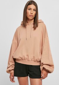 Kerge roosa ülisuur kapuutsiga hoodie, millel on nööriga kapuuts, soonikkoes äär ja laiad varrukad, kombineeritud mustade lühikeste pükstega. Pehme kangatunne.