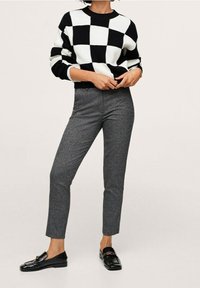 Zwart-wit geruite trui met ribbelstructuur, gecombineerd met op maat gemaakte grijze broeken. Zwarte loafers met een kleine hardwareaccent.