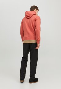 Roze hoodie met een trekkoord capuchon, geribbelde manchetten en zoom. Gecombineerd met zwarte broeken en donkere schoeisel, gezien van achteren.
