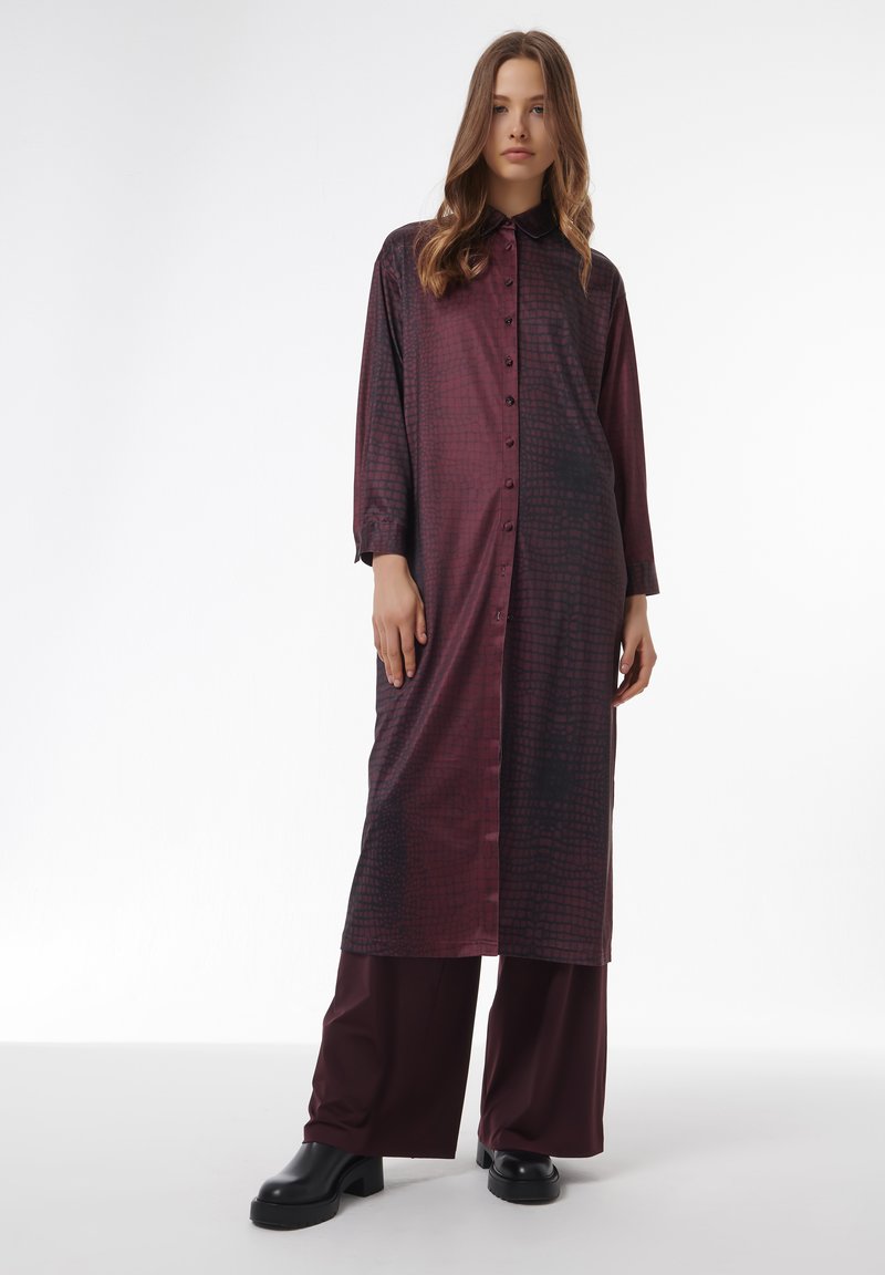 Bordeaux rood shirtjurk met een gestructureerd patroon, lange mouwen en een kraag. Gecombineerd met wijde bordeaux broek en zwarte platform schoenen.