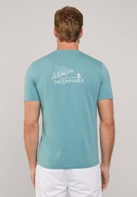 Camiseta de manga corta en algodón de color azul claro con un gráfico en la parte posterior que presenta un diseño de palmera y la marca en letras blancas.