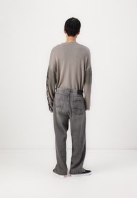 Sivkasto pleteno pulover s širokimi rokavi, v kombinaciji z ohlapnimi sivimi jeans hlačami, ki imajo zadnji žep in črno etiketo, obutimi v črne superge.