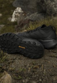 Chaussures de trail running noires avec semelles en caoutchouc Continental texturées reposant sur de la terre et de l'herbe en extérieur.