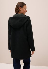 Veste en polaire noire avec capuche, dotée d'une surface texturée et d'une coupe légèrement oversized, présentée sur un fond neutre.