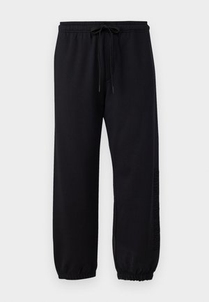 Black sweatpants made of soft fabric, featuring an elastic waistband with a drawstring, cuffed ankles, and embossed text along one leg.