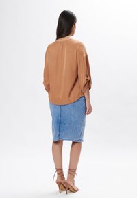 Blusa marrone leggera con orlo arrotondato e vestibilità ampia, abbinata a una gonna di denim blu aderente. Sandali alti con cinturini color sabbia completano il look.