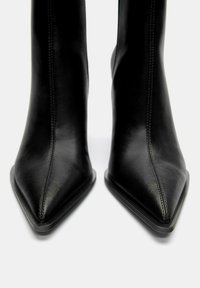 Stivali in pelle nera alla caviglia con punta affusolata, design elegante e dettagli di cucitura discreti lungo le cuciture, dotati di una suola a profilo basso.