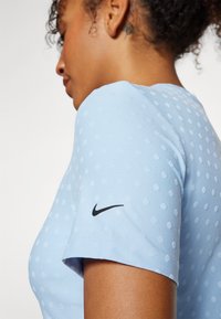T-shirt de sport bleu clair avec un motif de pois texturé. Présente le logo noir de Nike sur la manche. Manches courtes et encolure ronde.