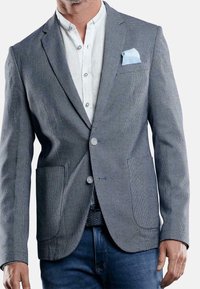 Szary blazer w wzory z dwoma przednimi kieszeniami, noszony na białej koszuli zapinanej na guziki, z jasnoniebieską chusteczką w kieszeni i teksturowanym wykończeniem.