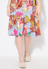 Vestido midi floral con fondo azul, que presenta patrones vibrantes en rojo, rosa y verde. Acompañado de bailarinas de ganchillo beige con adornos.