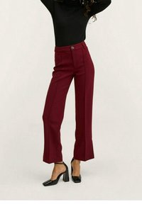 Pantalon taille haute bordeaux à coupe ajustée, avec coutures latérales et taille boutonnée. Associé à des chaussures noires à talons hauts.