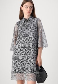 Robe en dentelle grise avec un col, des manches évasées et des motifs floraux. Les détails notables incluent une demi-fermeture éclair et un ourlet en dentelle.