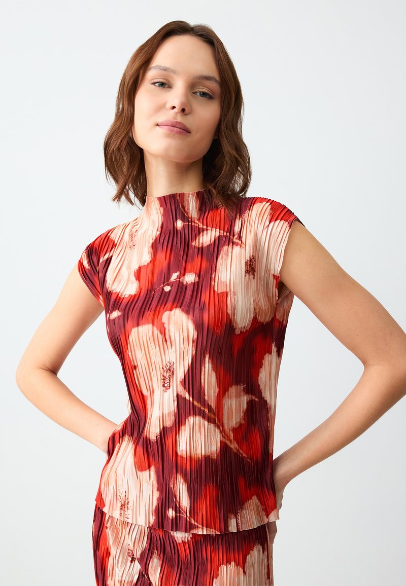 Top plissettato rosso e beige con collo alto e maniche a sbuffo, caratterizzato da una stampa floreale con forme astratte. Texture liscia, design aderente.
