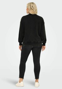 Svart oversized sweatshirt med ribbstickade ärmar och nederkant, ihop med mörka skinny jeans med fransade nederkanter och vita sneakers.