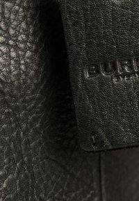 Zwart leer met een gestructureerd oppervlak en een prominente label met reliëflettertype. Het etiket is bevestigd met een gestikte afwerking.