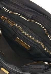 Interno di una borsa a tracolla in pelle nera con cerniere dorate, molteplici scomparti e un'etichetta che recita "CATERINA LUCCHI MADE IN ITALY."