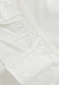 Weißer Stoff mit gerüschtem Rand, der gestickte Blumenmuster aufweist. Glatte Textur mit dezenten Designakzenten.