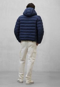 Giacca puffer blu navy con leggero trapuntato orizzontale e cappuccio, abbinata a pantaloni cargo bianchi con tasche laterali e una vestibilità comoda.