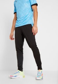 Hellblaues, atmungsaktives Sportshirt aus Mesh, schwarze, zulaufende Hose und bunte Turnschuhe mit einer Mischung aus rosa, gelben und blauen Akzenten.