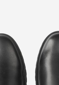 Bottes en cuir noir avec des orteils arrondis, texture lisse et coutures subtiles le long du bord. Design épuré, accents minimalistes.