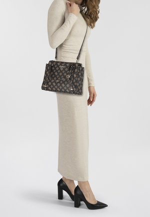 Czarna torebka w wzory ze złotymi akcentami, w kształcie prostokąta, z odpinanym paskiem na ramię i zamkiem błyskawicznym. Noszona przez osobę w neutralnej sukience.