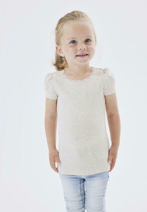 Hellbeige geripptes Strickoberteil mit kurzen Puffärmeln und einem gewellten Ausschnitt, kombiniert mit hellblauen Skinny-Jeans.