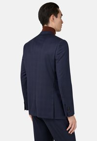 Chaqueta de traje azul marino hecha de tela texturizada con un patrón de cuadros. Presenta solapas de muesca y puños abotonados, mostrando un ajuste a medida.