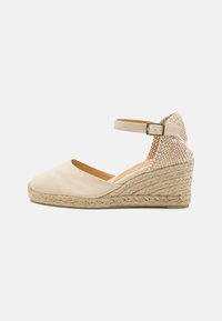 Beige canvas wedge espadrille with a textured back panel, ankle strap, and braided jute outsole. Rounded toe and flat heel.