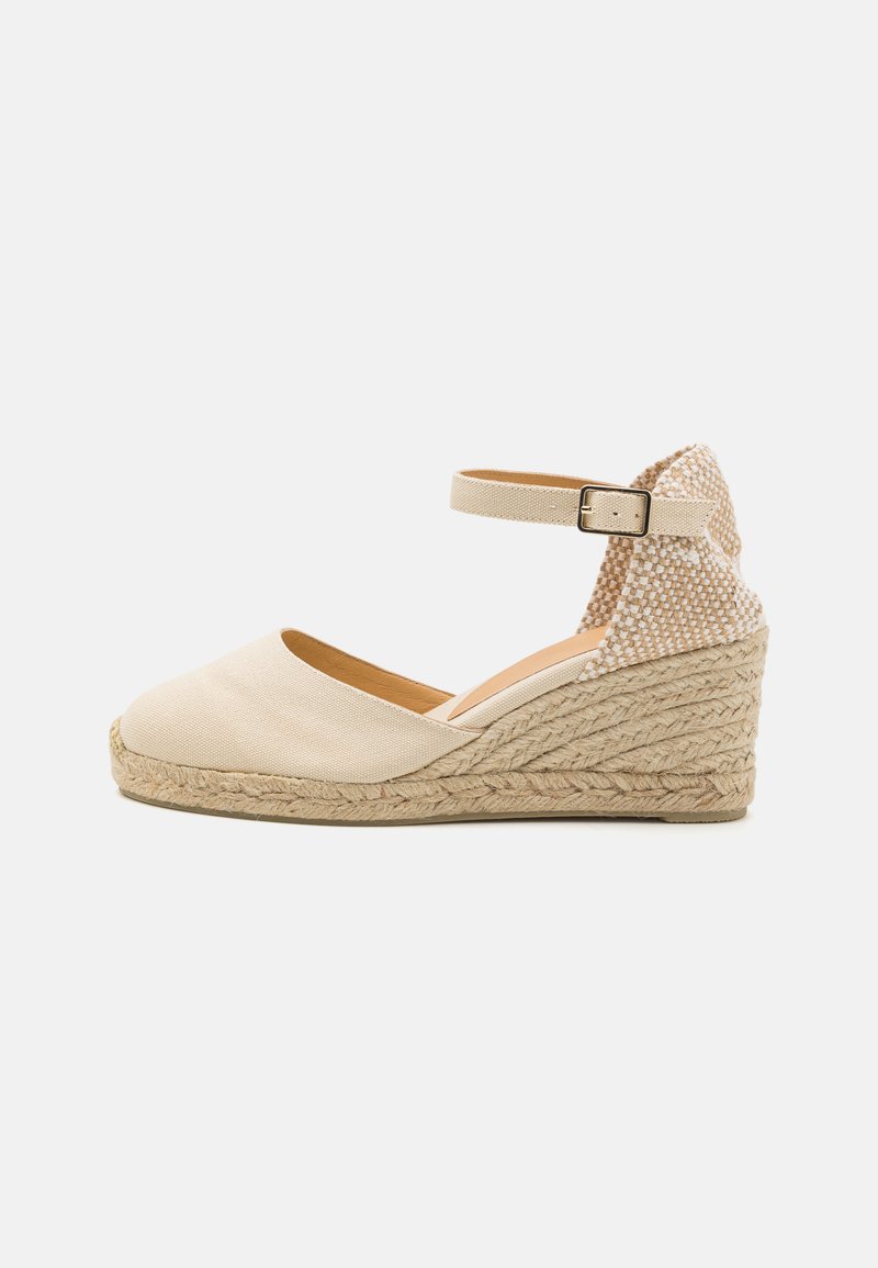 Beige canvas wedge espadrille with a textured back panel, ankle strap, and braided jute outsole. Rounded toe and flat heel.