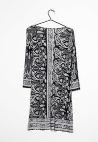 Svart och vit paisleyklänning med trekvartsärmar, mönstrad tyg, rund halsringning och rak skärning, hängande på en svart krok.