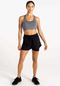 Sujeta deportiva gris con diseño de malla, combinada con pantalones cortos negros con cordón. Zapatillas deportivas negras complementan el atuendo. De pie sobre un fondo neutro.