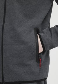 Geverfd grijs stoffen jack met een zwart ritszakje, contrasterende accenten en een trekband met rode details. Slim fit ontwerp.