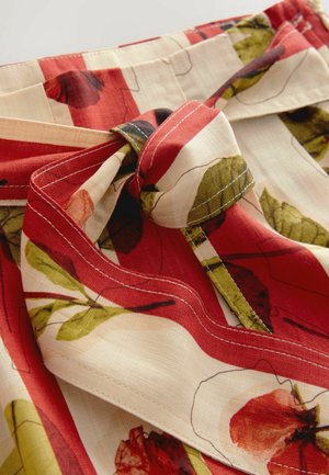 Rood met bloemenpatroon stof met groene bladeren en een crèmekleurige achtergrond. Bevat een gestrikte knoopdetail en contrasterende stiksels langs de randen.