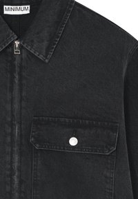 Black denim jacket featuring a collar, front zipper, and a chest pocket with a snap button. The fabric has a textured finish.