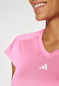 Tricou sportiv roz cu decolteu în V, mâneci scurte și un accent cu logo alb. Textură netedă, design ajustat, potrivit pentru activități sportive.