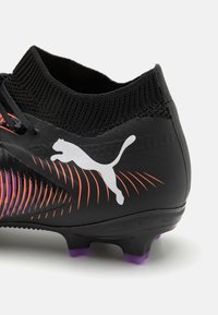 Melnas futbola kurpes ar teksturētu sintētisko virsotni, adītu apkakli, oranžs un violetas gradienta dizains, un baltu Puma logo. Violets pirksts.