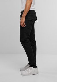 Jeans negre din denim, cu un croi slim, având două buzunare la spate și fermoar, asortați cu adidași albi. Finisaj texturat și neted.