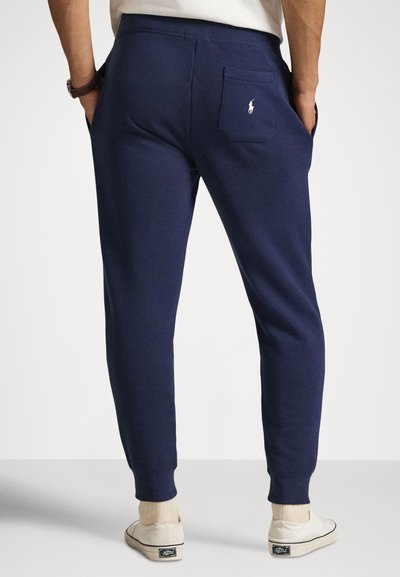 Tmavomodré teplákové nohavice z mäkkej tkaniny, s kužeľovitými nohavicami, rebrovanými manžetami a zadným vreckom s malým logom.