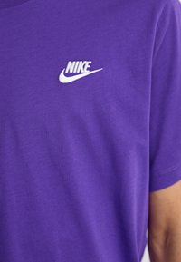 Lilla bomulds T-shirt med et hvidt broderet Nike-logo på venstre brystområde. Rund halsudskæring med korte ærmer.