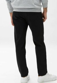 Schwarze Hose mit geradem Schnitt, ausgestattet mit Gesäßtaschen. Hergestellt aus weichem Stoff, kombiniert mit weißen Sneakern für einen lässigen Look.