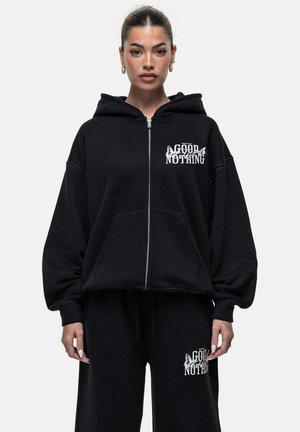 Felpa nera con zip realizzata in un tessuto morbido, dotata di una tasca frontale e testo grafico sul lato sinistro del petto. Vestibilità ampia con cappuccio.