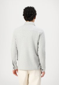 Sweatshirt gris avec un col, des manches longues et des poignets boutonnés. Fabriqué en matériau doux avec une finition texturée. Design simple.