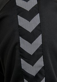 Schwarzer Stoff mit vertikalem Streifenmuster aus abwechselnden schwarzen und weißen Chevron-Mustern in strukturiertem Material.