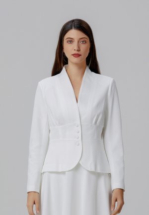 Blazer blanc au design ajusté, avec un col châle, des boutons à un rang et une texture lisse. Associé à une robe blanche assortie.