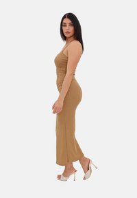 Abito maxi a coste color sabbia con un design aderente, spacco laterale e spalline sottili, abbinato a mule con tacco alto color crema con un motivo testurizzato.