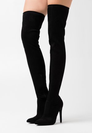 Botas negras hasta el muslo hechas de suave ante, con tacón de aguja, puntera afilada y detalle de cremallera lateral. Textura suave en toda su superficie.