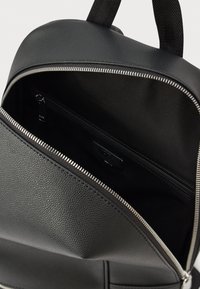 Mochila de cuero negro con compartimento principal con cremallera, textura suave y un bolsillo interior adicional. Cuenta con herrajes plateados.