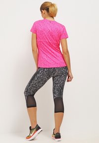 Camiseta deportiva rosa ajustada combinada con leggings capri de patrón en blanco y negro, que cuentan con paneles de malla y zapatillas deportivas de colores.